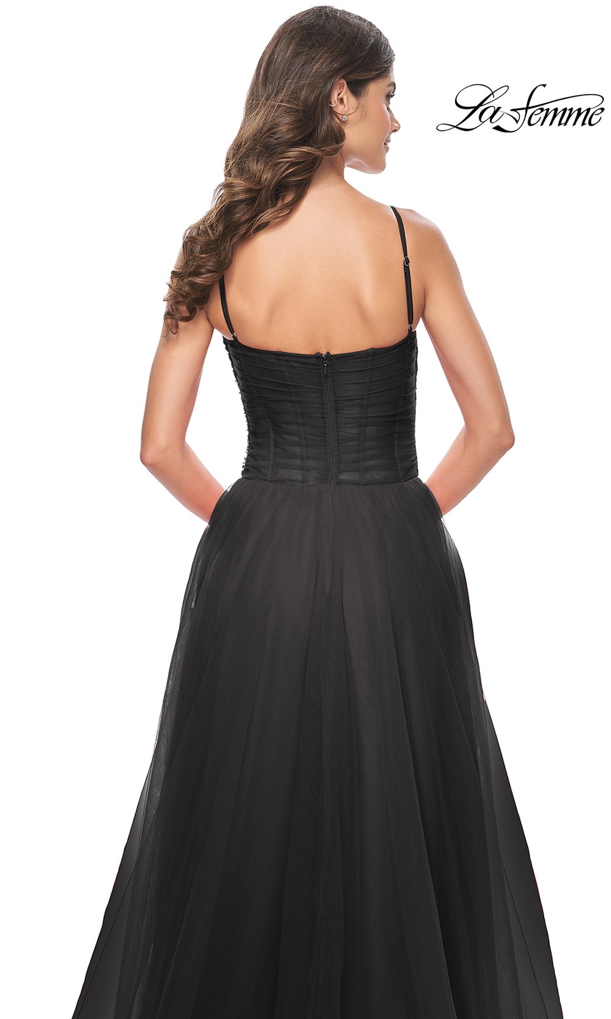 A woman with long wavy hair models the La Femme Sheer-Waist Long Prom Ball Gown 32017, a black, strapless A-line dress with a fitted bodice and flowing skirt, shown from the back. The La Femme logo appears in the top right corner.